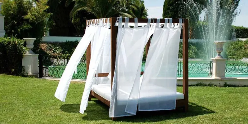 Cama balinesa de madera con cortinas blancas en un jardín
