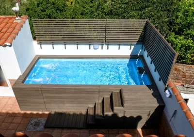 Vista aérea de una piscina elevada forrada con madera tecnológica marrón, con escalera y celosía, en Badajoz