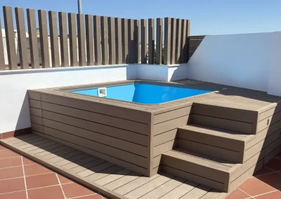 Piscina elevada pequeña forrada con madera tecnológica gris pardo, con escalera y tarima, en una terraza de Sevilla