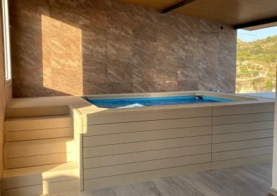 Piscina elevada forrada con madera tecnológica en tono crema bajo un porche, con escalera lateral, en Alicante