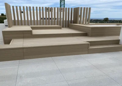 Piscina elevada con tarima en dos niveles, escalones y celosía de madera tecnológica clara en una terraza de Málaga