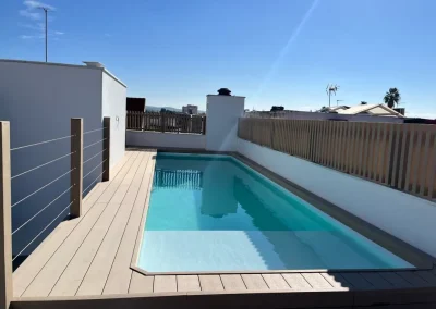 Piscina en una terraza de Córdoba rodeada de tarima de madera tecnológica clara, con valla de lamas verticales y barandilla de cables