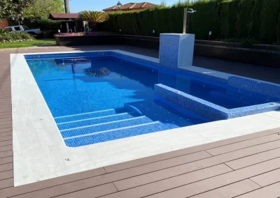 Tarima marrón de madera tecnológica junto a la coronación blanca de una piscina de gresite
