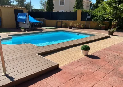 Tarima marrón de madera tecnológica alrededor de una piscina en un jardín, con escalón rematado