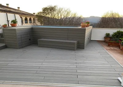 Terraza con tarima gris y piscina elevada forrada con banco y escalera de madera tecnológica