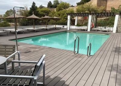 Tarima de madera tecnológica alrededor de una piscina con tumbonas y pérgola