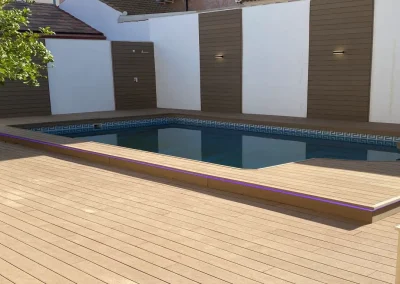 Tarima de madera tecnológica con tira LED en el borde de la piscina y paneles a juego en la pared