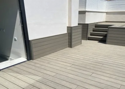 Terraza con tarima gris, escalones y zócalo de madera tecnológica en la pared