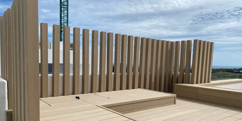 Celosía de lamas verticales de madera tecnológica clara en una terraza con piscina