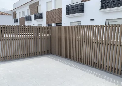 Valla de lamas verticales de madera tecnológica cerrando un patio